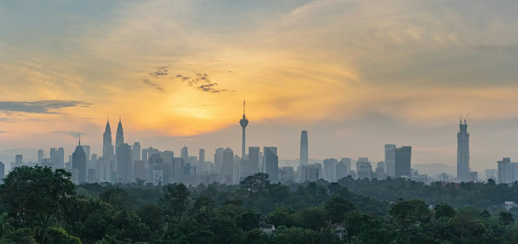 Kuala Lumpur skyline at sunrise above a green tree canopy