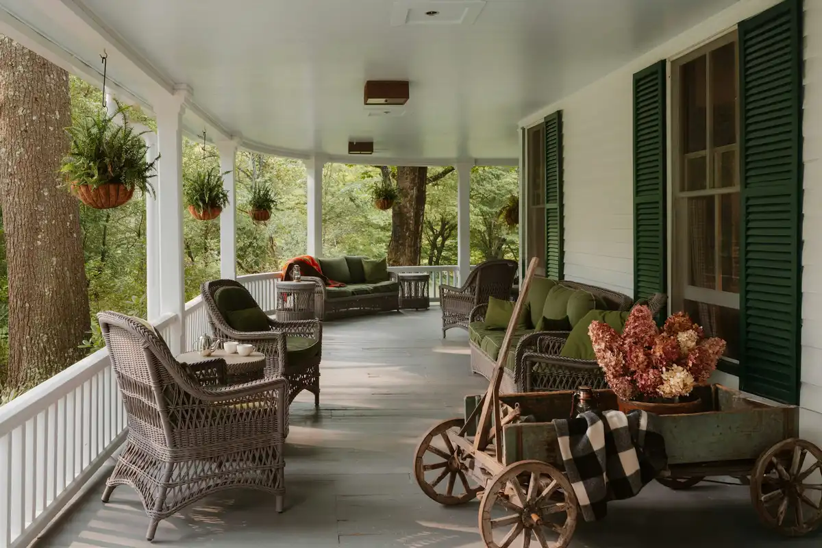 Long covered veranda with wicker armchairs, cushions and hanging ferns, trees beyond the railing